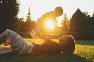 Young mother and baby playing in park at summer. Beautiful mom and child outdoors. Parent with kid...