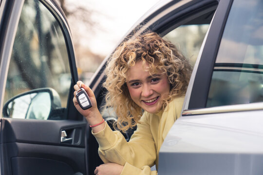 Smiling Caucasian woman driver sits in the new car and shows car keys copy space portrait . High quality photo