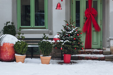 Three green decorative Christmas trees stand in pots on the snow near a store with green doors in...