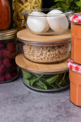 Closeup view of three glass jars piled with wooden covers full of eggs, quinoa and spinach next to more delicious food.