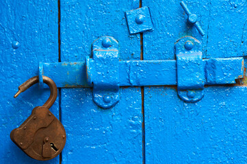 An old wood blue painted door with metal rusted latch, padlock and antique door handle