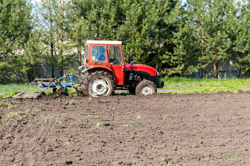 Modern red tractor machinery plowing agricultural field meadow at farm at spring autumn. Farmer cultivating and make soil tillage before seeding plants and crops, nature countryside rural scene