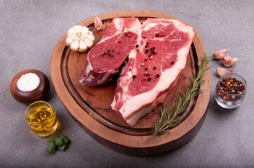 cut of raw meat with fat t-bone steak in the butcher's shop on wooden board with seasonings garlic olive oil