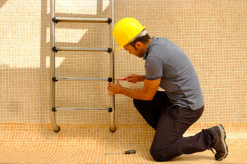 worker installing pool ladder in an empty swimming pool under construction © Marcos