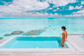 Luxury resort travel vacation destination idyllic overwater bungalow villa woman relaxing by infinity pool. Social media influencer traveler luxurious high end lifestyle