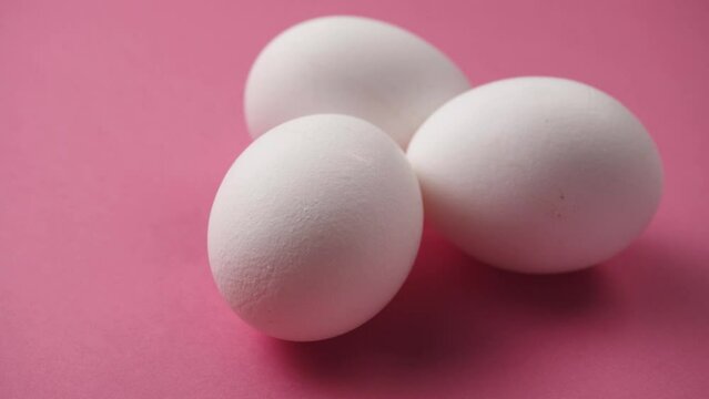 Eggs rotate on pink background. Close-up of three fresh, organic and healthy chicken egg. White Eggs are rolling on the clean pink table. Easter eggs background.