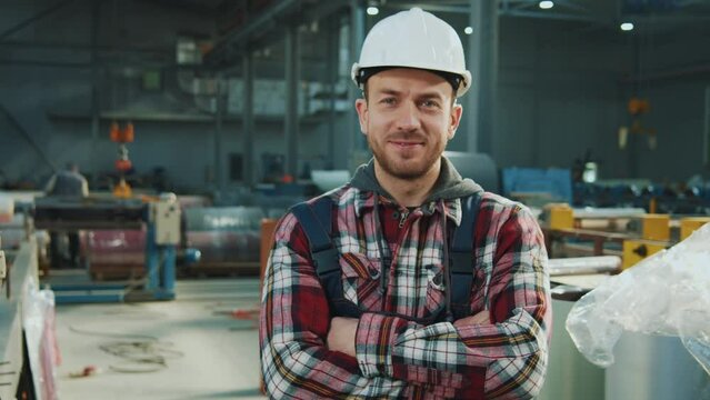 Handsome industry engineer man wears safety uniform and hard hat stand look at camera smiling feel happy in factory. Inspector in warehouse.