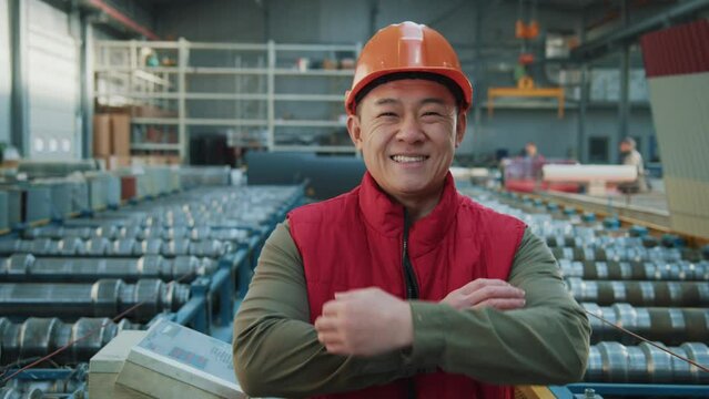 Smiling happy asian engineer man wearing safety uniform and hard hat stand look at camera in factory. Inspector in warehouse.