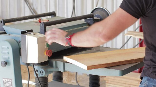 young carpenter working on a Thickness Planer machine cutting a wooden board in a carpentry workshop using safety glasses