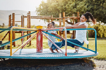 The fun all happens at the park. Portrait of a mother and her daughter playing together on a merry-go-round at the park.