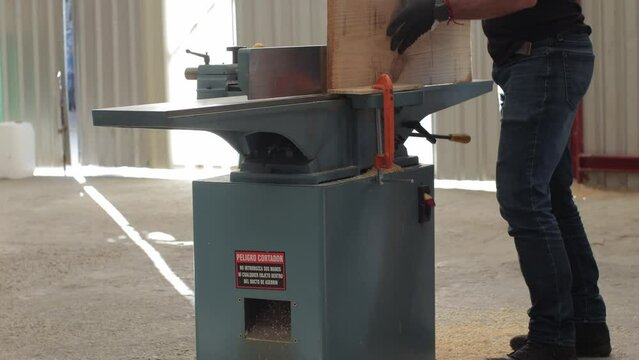 young carpenter working on an Electric Benchtop Jointer machine cutting a wooden board in a carpentry workshop using safety black gloves