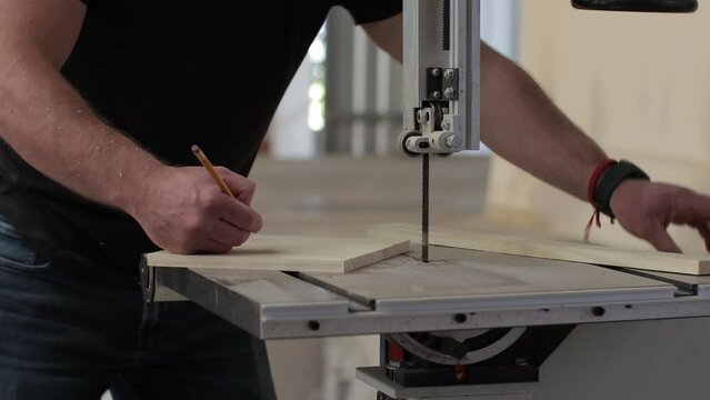 young carpenter working on a teble saw machine marking and cutting a wooden pllank in a carpentry workshop