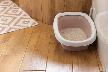 Cat toilet with filler in the interior of the bathroom with white tiles and imitation wood tiles.