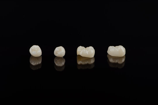 Qualified anatomic ceramic and zirconia crowns of human teeth close up macro isolated on black background.