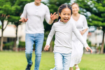 Naklejka na ściany i meble Portrait of enjoy happy love asian family father and mother run with cute little asian girl child smiling play and having fun moments good time in summer park at home