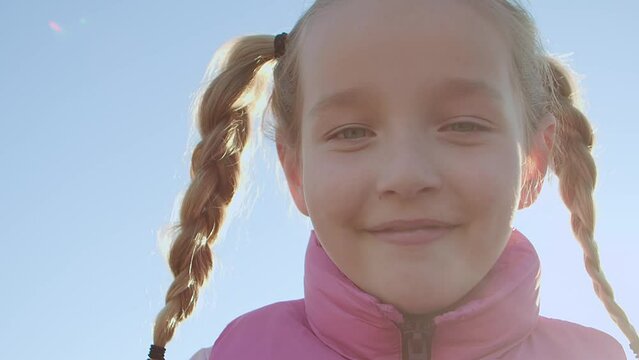 A small braided blonde smiles at the camera and reveals the gaps between her teeth.
