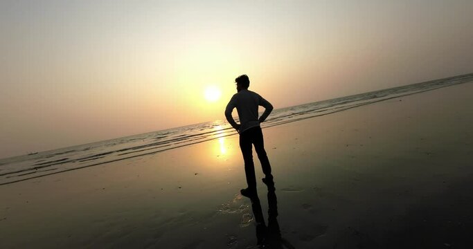 boy walking in beach side and feel this view reflection  on sand India Mumbai in the sunset