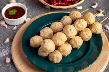 Fried pork meatballs skewers bamboo on a green plate with spicy sauce on a table,
fried pork tendon meatballs Thai street food.