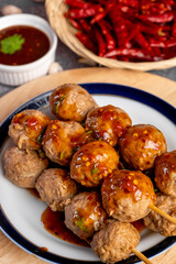 Fried beef meatballs skewers bamboo on a white plate with spicy sauce on a table,
fried beef tendon meatballs Thai street food. 