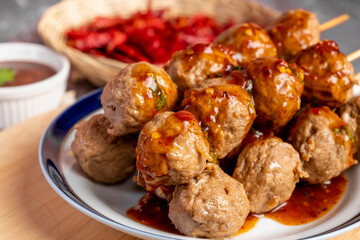 Fried beef meatballs skewers bamboo on a white plate with spicy sauce on a table,
fried beef tendon...