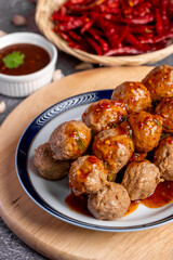 Fried beef meatballs skewers bamboo on a white plate with spicy sauce on a table,
fried beef tendon meatballs Thai street food. 