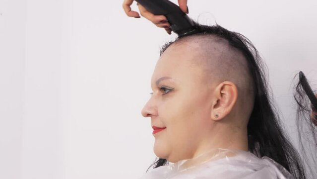 A brunette woman hairdresser shaves her head with a machine, she rejoices. medium plan