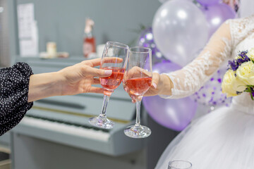 Cropped hands of young girls, brides and girlfriends, hold glasses of wine in their hands and hit each other, clink glasses.