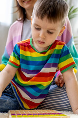 Montessori material. Woman and a boy study at a home school. Mom and son in rainbow clothes