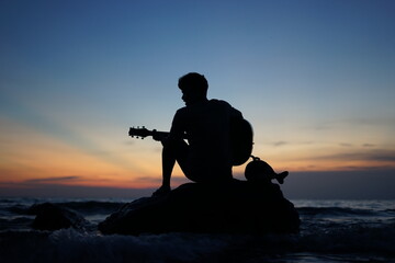 Fototapeta na wymiar A man playing guitar on rocks with the silhouette.