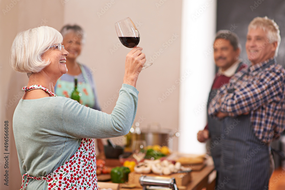 Wall mural She always serves the finest vintages. Shot of a senior woman looking at her wine with friends in the background.