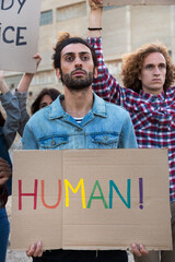 Naklejka na ściany i meble Young arab man protesting on a demonstration for LGBT rights holding cardboard banner. Vertical image.