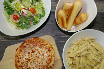 View of a full Italian meal with pizza, salad, alfredo pasta and breadsticks.