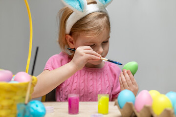 Little child in Easter bunny ears painting colored eggs. Holiday preparations at home and craft concept.