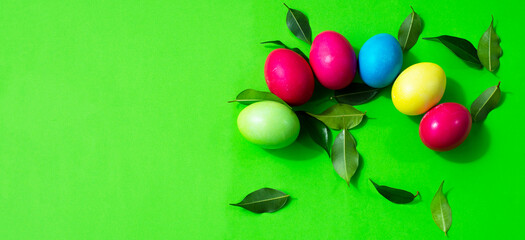 Eggs painted in different colors and a scattering of green leaves on a green background. Copy space for text. Postcard.