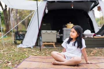 Asian child cute or kid girl camper sitting on mat and grass lawn on nature camping tent or cabin...