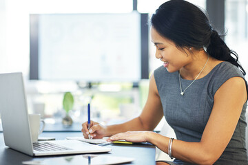 Putting plans into perspective and on paper. Cropped shot of a young businesswoman writing notes while working on a laptop in a modern office.