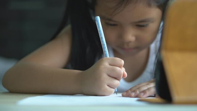 closeup hand asian child back to school or kid girl write or drawing learning by pencil on book and computer tablet with homework to video call or people learn from home and study online on smartphone
