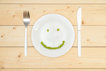 The concept of healthy eating, green peas laid out on a white plate in the shape of a smile. Top...
