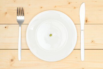 One green pea on a white plate standing on a wooden background, top view