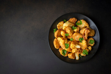 Fried in batter Cauliflower florets served on a black plate on a grey concrete table with ingredients, view from above, close-up, flatlay, copy space (Turkish name; karnabahar kizartmasi)