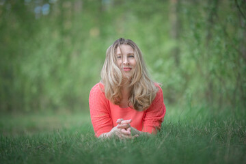 Fototapeta premium Beautiful blonde young woman in a pink blouse in the park.