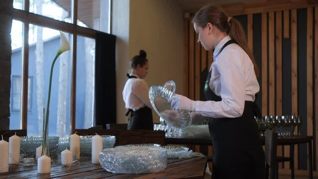 Two waiters preparing to serve table for celebration. Women in uniform wiping and polishing crystal glass plates in restaurant. Catering concept