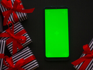 Mock up on smartphone and presents. Gifts in a stripped wrapper and with red ribbons on the dark corrugated cardboard with copy space. Christmas sale shopping. Black Friday and Cyber Monday.