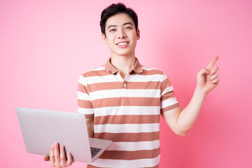 Portrait of young Asian man using laptop on pink background