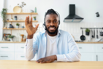 Headshot portrait of African American man in headset using laptop computer webcam for chatting online, video call concept, greets, looking at the camera and smiling friendly