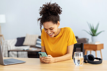 Young African American woman using mobile phone, chatting online sitting at a desk in a home...