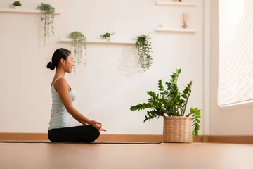 Fototapeten Calm of wellness Asian young woman sit on yoga mat doing breathing with yoga lotus pose.Yoga meditation of young healthy woman relax and comfortable at white cozy home,Yoga Exercise Wellness Concept © 220 Selfmade studio
