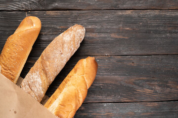 Three crispy french baguettes on a wooden background in a paper bag. view from above. Copy space