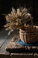 Still life with a bouquet of wheat in a wicker basket on a wooden table.
