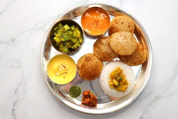 Indian vegetarian Thali or platter includes Aloo ki sabji, dal rice, Puri bhaji, Shrikhand or Srikhand, Aamras, papad, pickle, and chutney. Mashed potato curry or masala. Indian Festival food Thali.